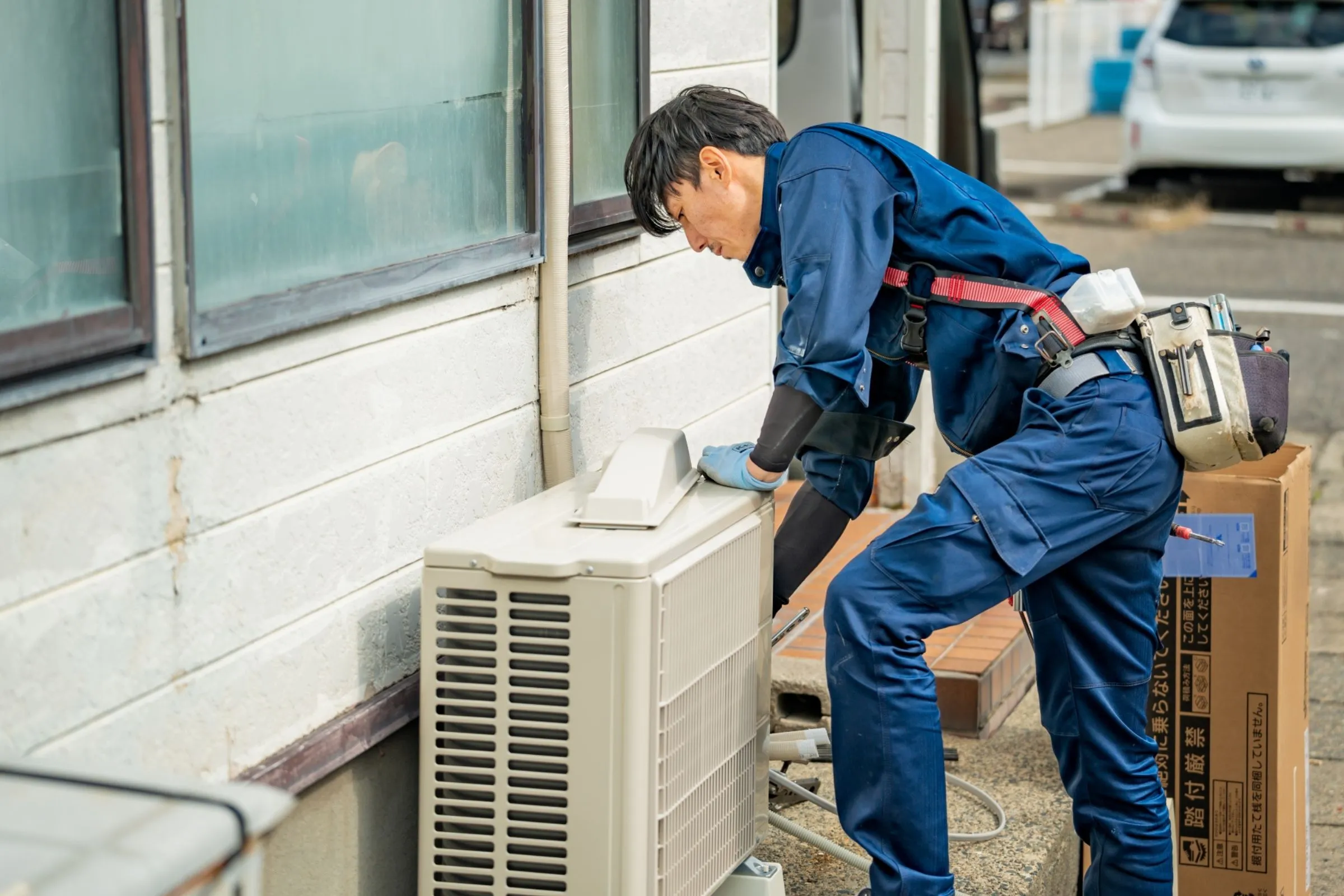 住宅の外で室外機を点検する若手の作業員。建設業の採用ページで伝える仕事の様子